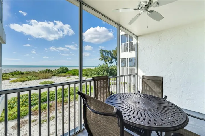 Balcony featuring a sunroom, view of water and beach, and ceiling fan