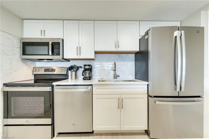 Kitchen featuring appliances with stainless steel finishes, white cabinetry, decorative backsplash, and light stone countertops