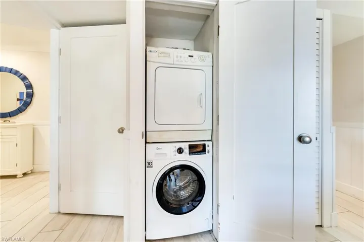 Washroom featuring estacked washer and dryer, wood finish floors, and wainscoting