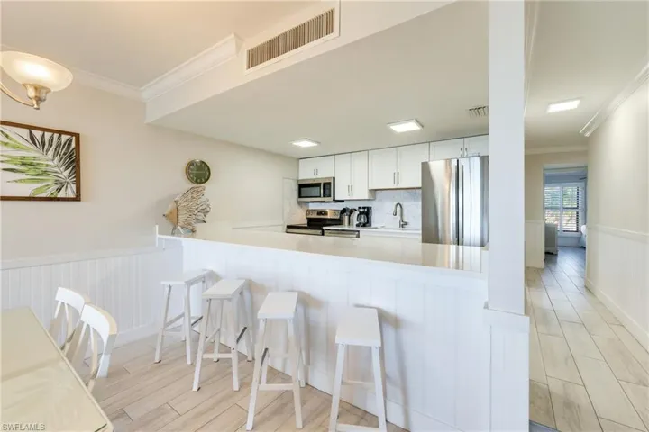 Kitchen featuring ornamental molding, a wainscoted wall, stainless steel appliances, wood finish floors, and white cabinetry