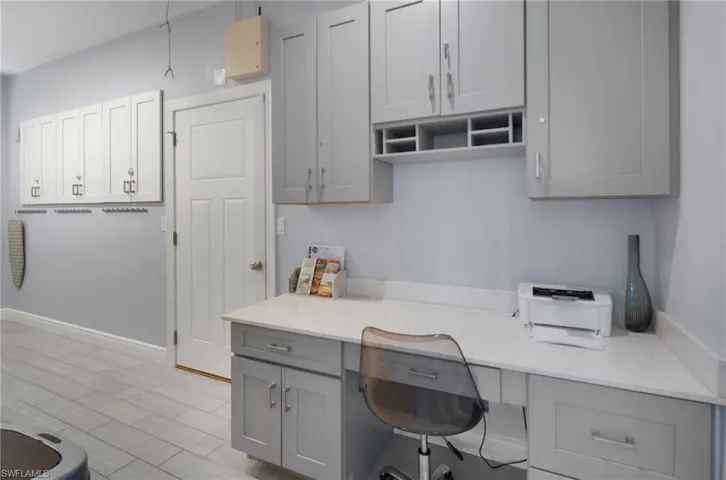 Dedicated workspace featuring a built-in desk with a light-toned countertop, integrated cabinetry, and overhead storage