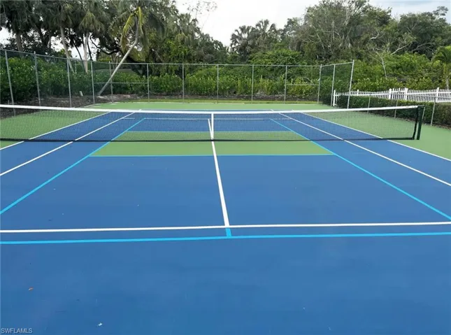 Private tennis court featuring a blue playing surface with green accents, white line markings, a black net, and a surrounding chain-link fence