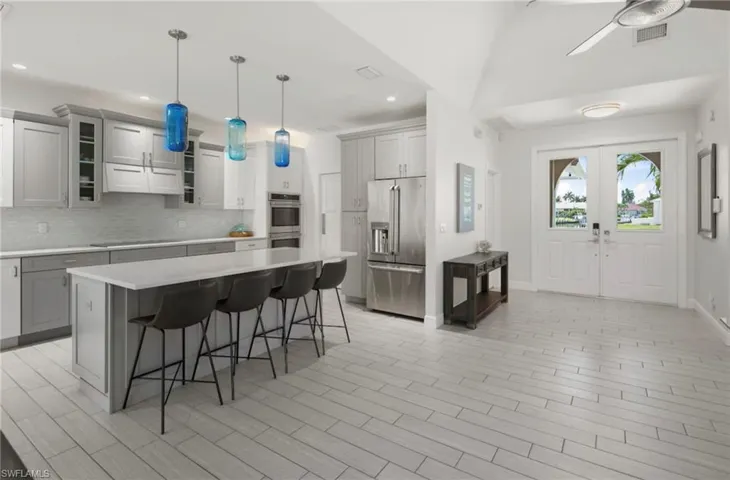 Open-concept kitchen featuring an oversized island with seating, stainless steel appliances, light-toned cabinetry, and a subway tile backsplash