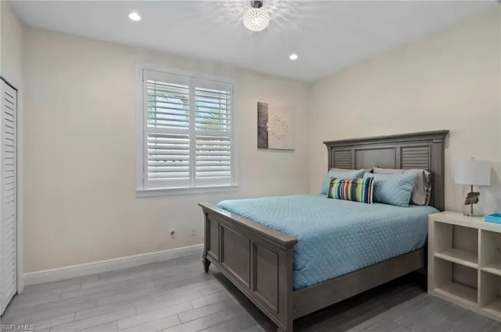 Interior room featuring wood-finish flooring, white walls, and a window with plantation shutters