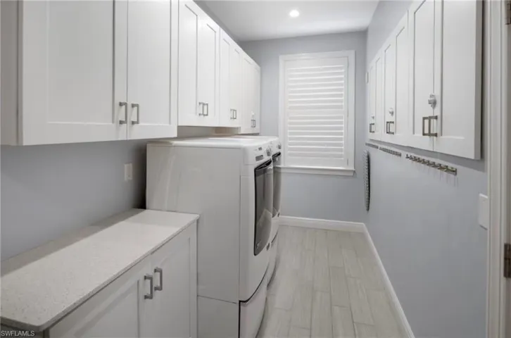 Dedicated laundry room featuring white shaker cabinetry, light-toned wood-finish flooring, and a window with plantation shutters