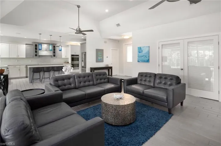 Open-concept living space featuring vaulted ceilings, wood-finish flooring, a kitchen island with seating, a tile backsplash, and double glass-paneled doors