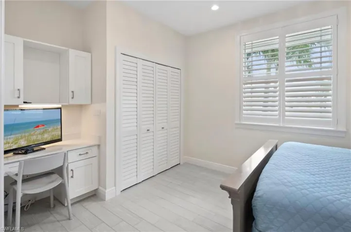 Built-in desk with overhead cabinetry, louvered closet doors, plantation shutters, recessed lighting, and wood-finish flooring