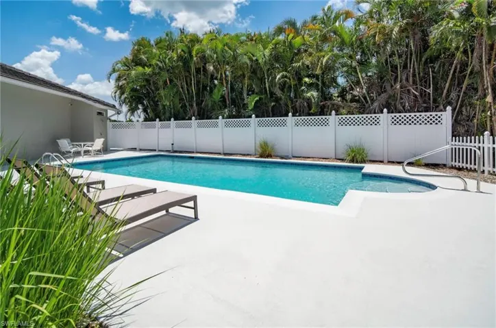 Rectangular swimming pool featuring a curved spa, white perimeter fencing, and concrete decking