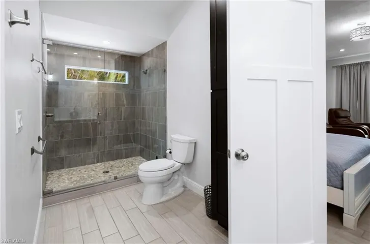 Spacious bathroom featuring a glass-enclosed shower with pebble flooring and stone-finish wall tile