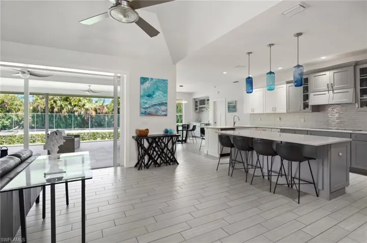 Spacious interior featuring light wood-finish flooring, high vaulted ceilings, and a kitchen with white and gray cabinetry, light countertops, and a full backsplash