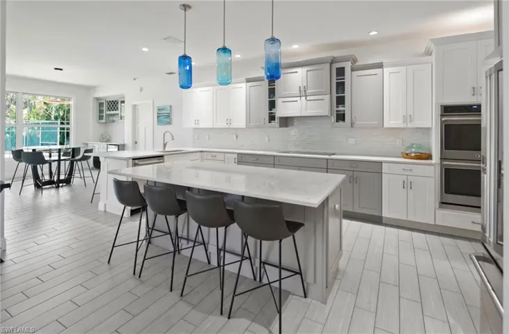 Spacious kitchen featuring a large island with seating, light wood-finish flooring, two-tone cabinetry, built-in double ovens, and a tile backsplash