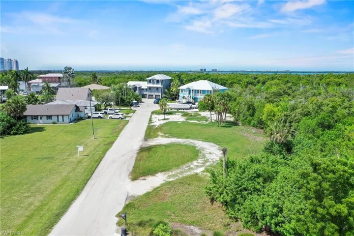 Expansive land parcel featuring a partially paved road access, mature trees, and existing residential structures nearby
