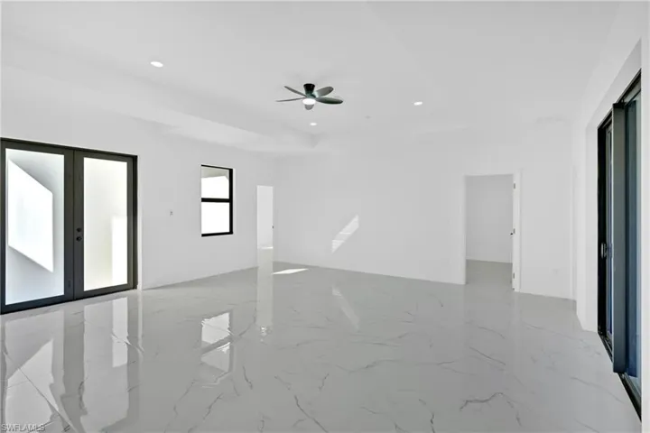 Empty room featuring recessed lighting, light marble finish flooring, a raised ceiling, a ceiling fan, and french doors