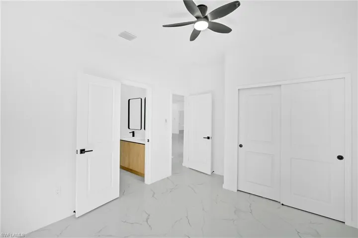 Unfurnished bedroom featuring ceiling fan, light marble finish flooring, and a closet