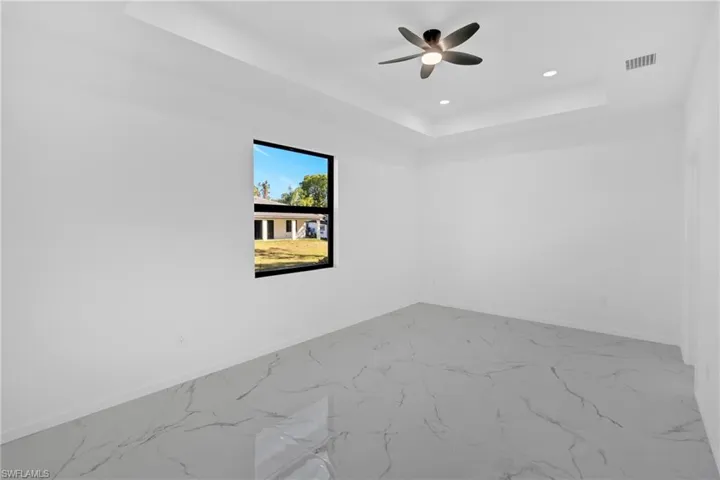Empty room featuring recessed lighting, a raised ceiling, marble look tiles, and ceiling fan