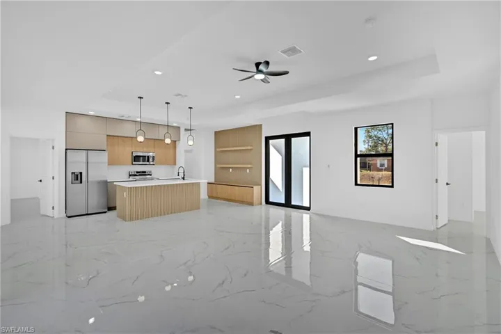 Kitchen featuring open floor plan, modern cabinets, light countertops, stainless steel appliances, and decorative light fixtures