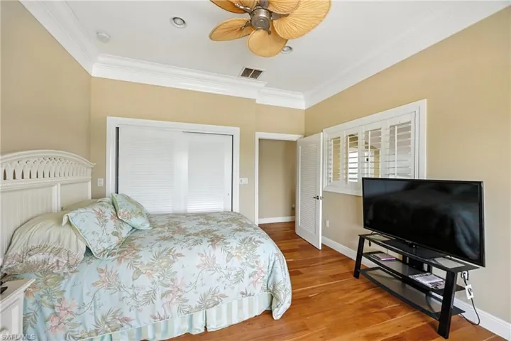 Bedroom with ornamental molding, wood finished floors, ceiling fan, and a closet