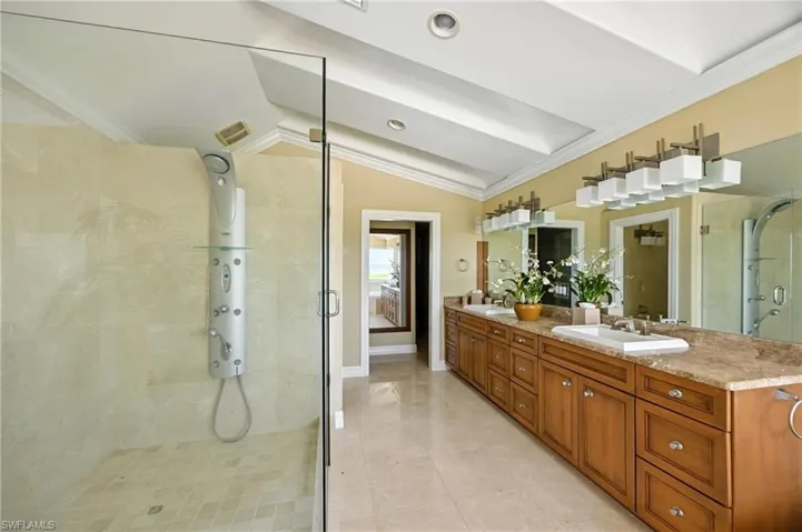 Bathroom with crown molding, a shower stall, double vanity, vaulted ceiling, and light tile patterned floors