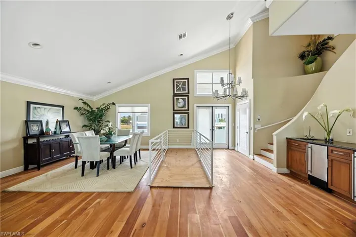 Dining room featuring ornamental molding, stairs, light wood-type flooring, plenty of natural light, and high vaulted ceiling