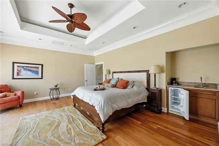 Bedroom featuring a raised ceiling, crown molding, wood finished floors, ceiling fan, and recessed lighting