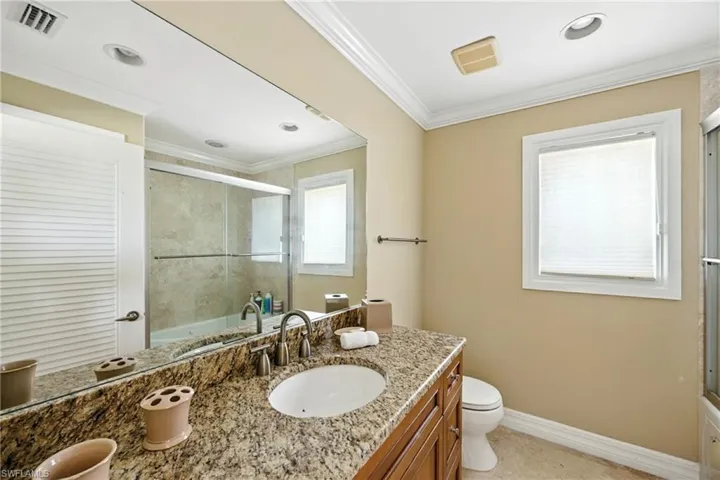 Bathroom with enclosed tub / shower combo, vanity, crown molding, light tile patterned flooring, and recessed lighting