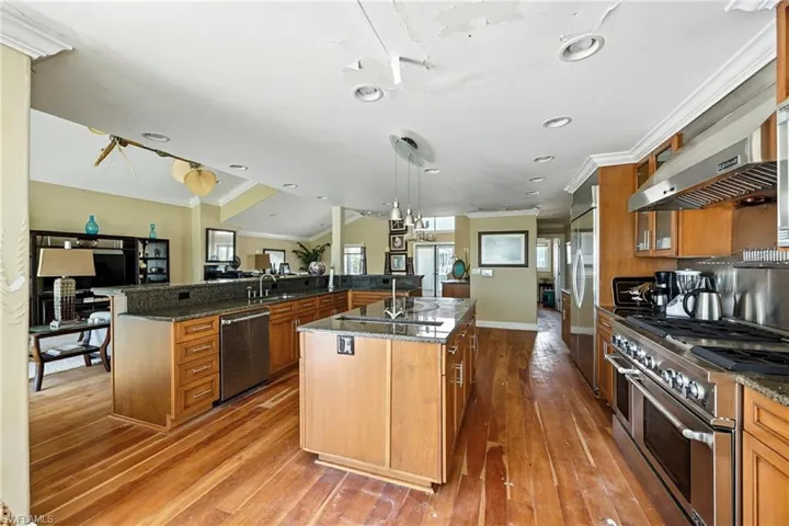 Kitchen with ornamental molding, premium appliances, dark stone countertops, open floor plan, and brown cabinets