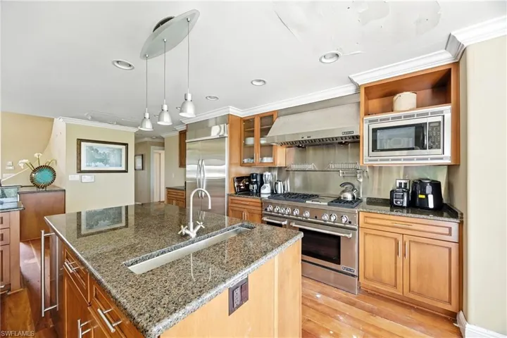 Kitchen with crown molding, light wood-style floors, built in appliances, dark stone countertops, and pendant lighting