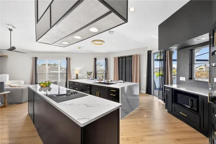 Kitchen with open floor plan, dark cabinets, light stone countertops, light wood-style flooring, and black appliances