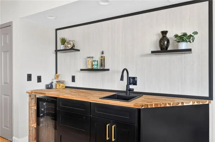 Indoor wet bar featuring dark cabinets, open shelves, butcher block countertops, and wine cooler