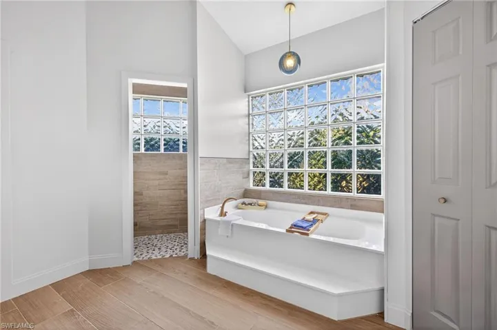 Full bath with a bath, lofted ceiling, walk in shower, a closet, and wood finish floors