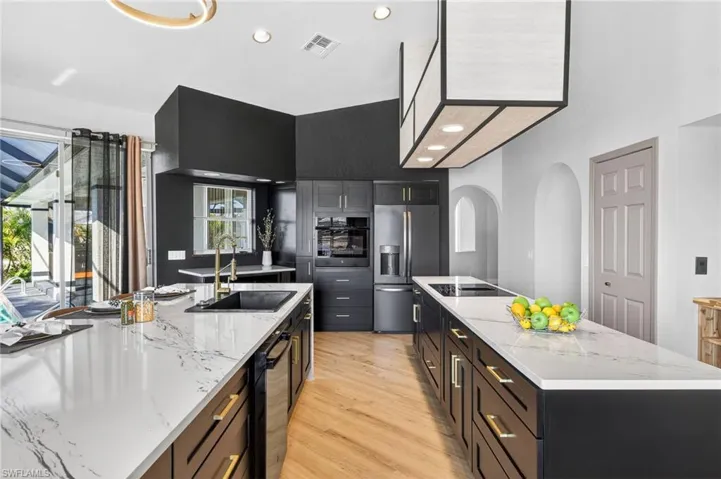 Kitchen featuring black appliances, light wood finished floors, recessed lighting, light stone countertops, and arched walkways