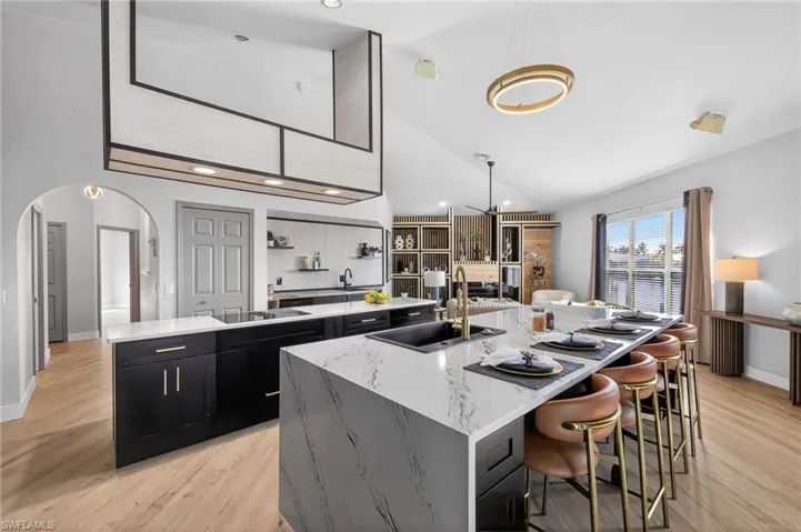 Kitchen with dark cabinets, light stone countertops, a kitchen bar, arched walkways, and light wood-type flooring