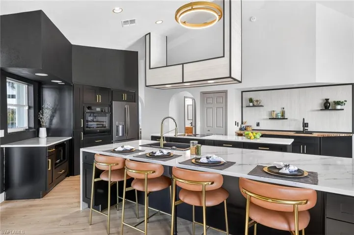 Kitchen featuring dark cabinets, arched walkways, light stone countertops, a kitchen breakfast bar, and stainless steel refrigerator with ice dispenser