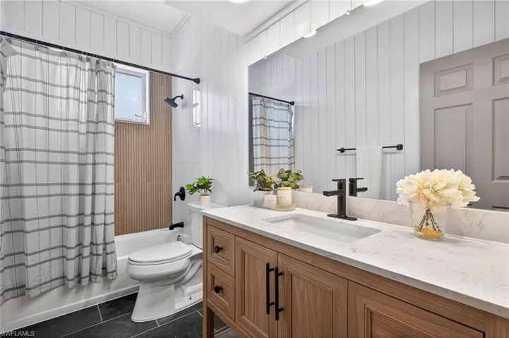 Full bathroom with shower / tub combo, vanity, dark tile patterned floors, and wood walls