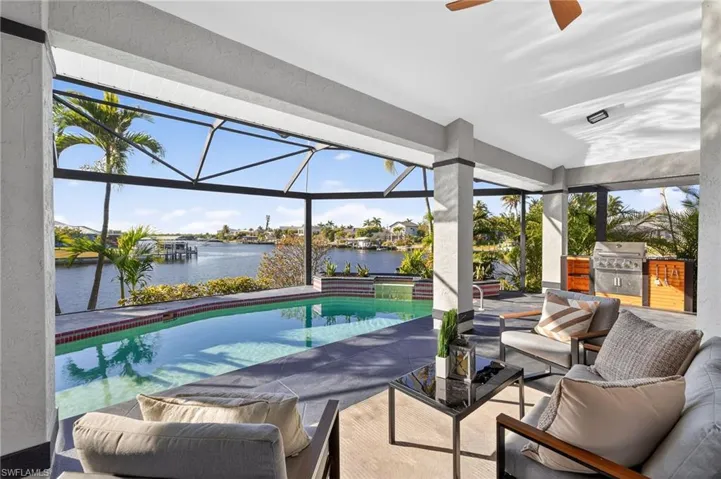 View of patio / terrace featuring a sunroom, a lanai, an outdoor kitchen with living area, a water view, and an outdoor pool