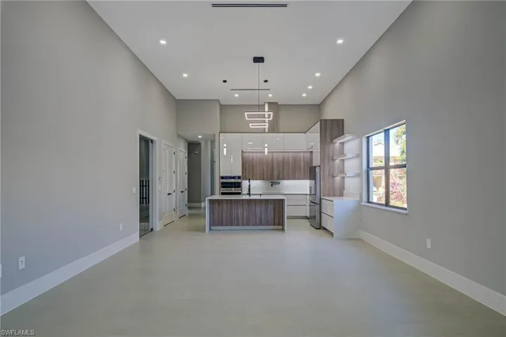 Kitchen featuring sink, hanging light fixtures, a kitchen island, stainless steel appliances, and a high ceiling