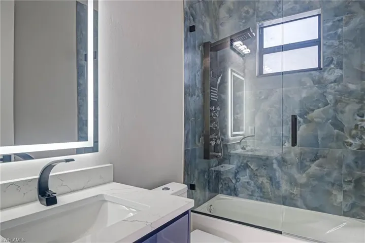 Full bathroom with vanity, bath / shower combo with glass door, and toilet