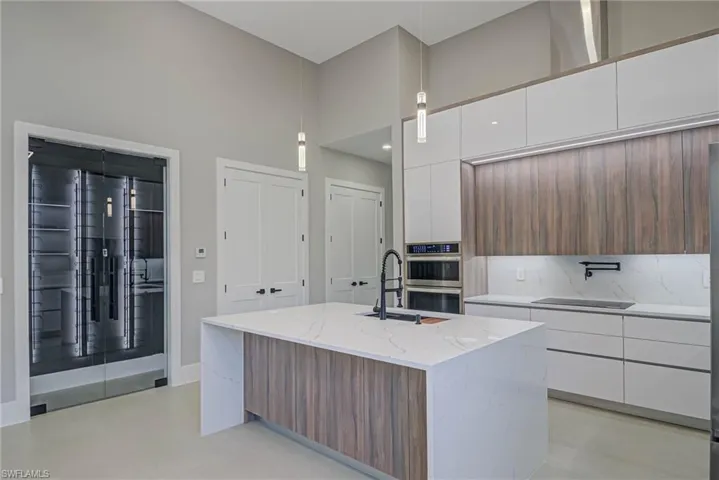 Kitchen with a kitchen island with sink, sink, pendant lighting, and white cabinets