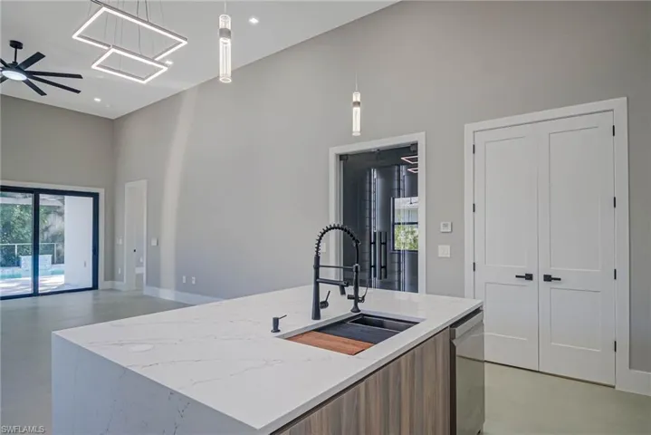 Kitchen with sink, dishwasher, a high ceiling, an island with sink, and decorative light fixtures