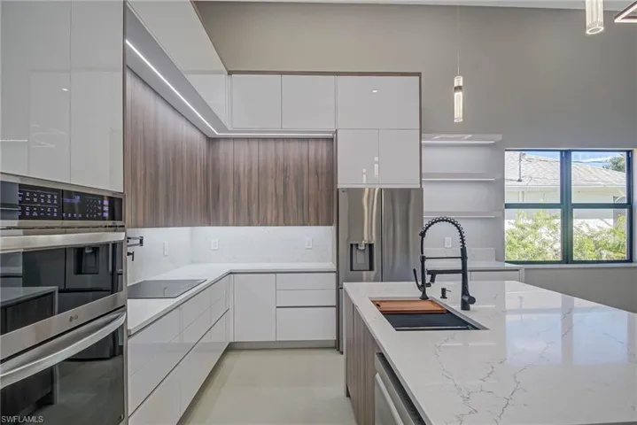 Kitchen featuring appliances with stainless steel finishes, decorative light fixtures, sink, white cabinets, and light stone countertops