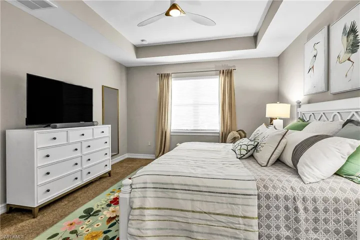 Bedroom with a raised ceiling, carpet floors, and ceiling fan