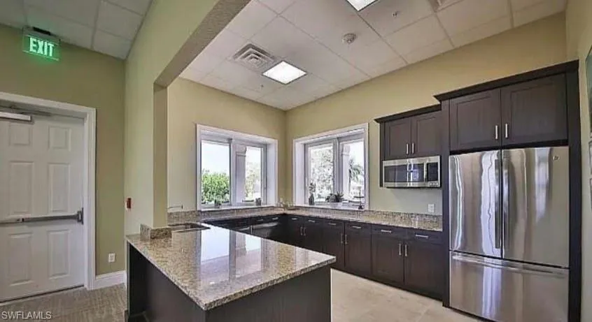 Kitchen with light stone countertops, stainless steel appliances, a paneled ceiling, a peninsula, and dark brown cabinetry