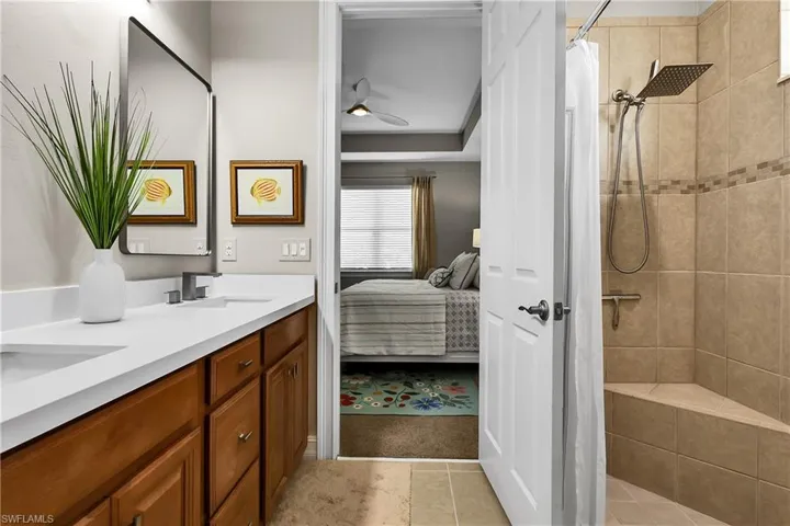 Full bath featuring tiled shower, double vanity, ensuite bathroom, ceiling fan, and light tile patterned floors