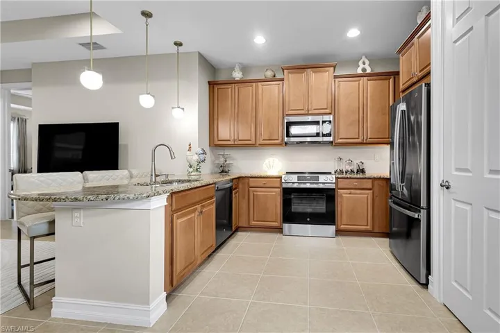 Kitchen featuring a kitchen bar, a peninsula, appliances with stainless steel finishes, hanging light fixtures, and light tile patterned flooring