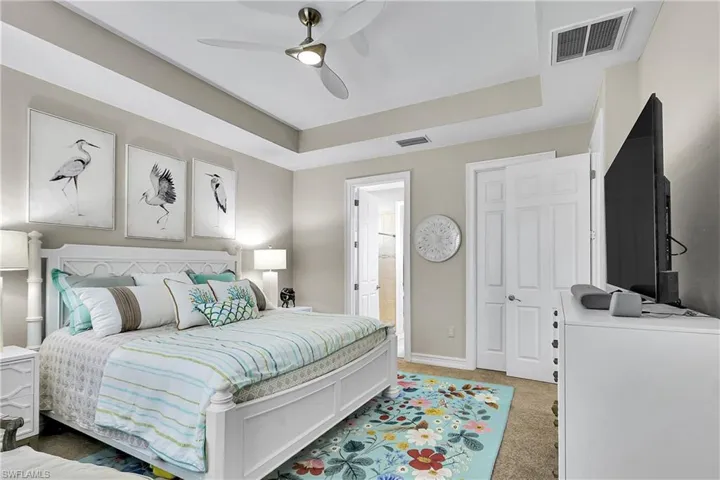 Carpeted bedroom featuring a tray ceiling, ceiling fan, and ensuite bath