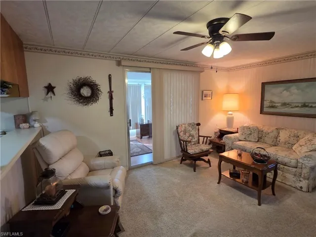 Living room with neutral carpet and ceiling fan. The Florida Room is through the sliding glass doors.