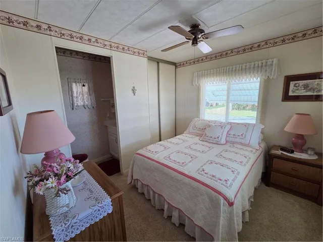 Bedroom with attached half bath, closet, neutral carpet, and ceiling fan.