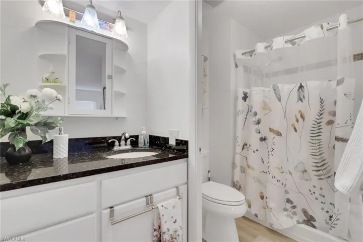 Bathroom featuring a dark speckled countertop, white vanity cabinetry, a built-in medicine cabinet with side shelving, and a shower-over-tub combination with a wall-mounted showerhead
