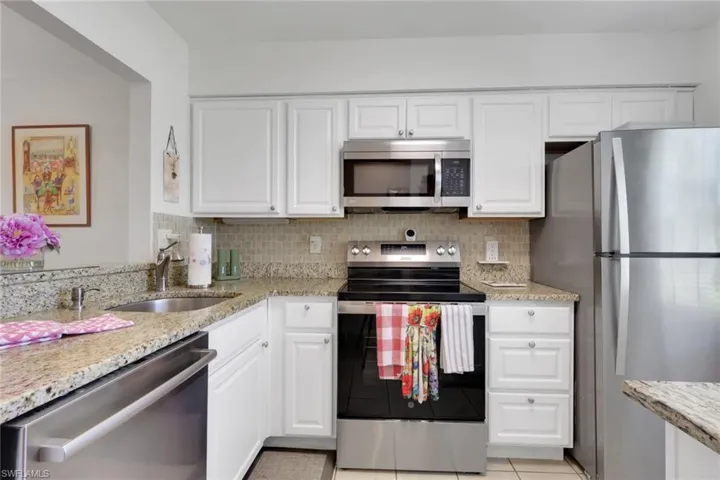 Kitchen featuring white cabinetry, granite countertops, a stainless steel sink, a tile backsplash, and stainless steel appliances