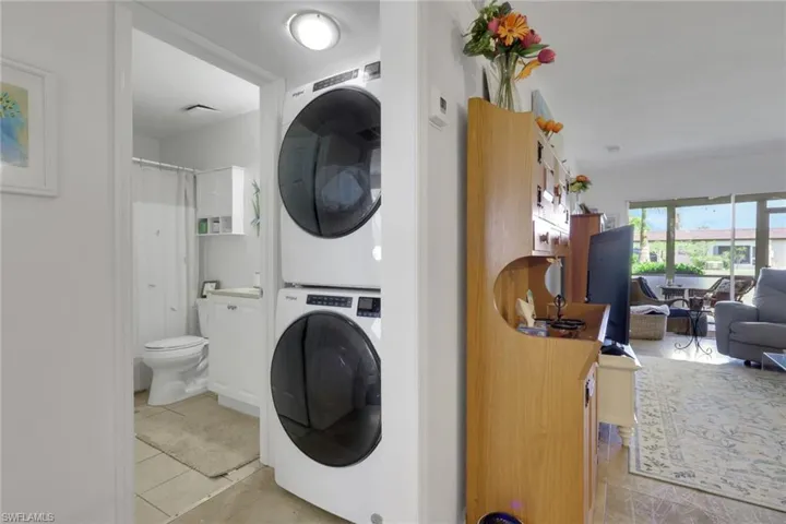 Compact laundry area featuring a stacked washer and dryer, adjacent to a full bathroom with a toilet and shower with shower curtain